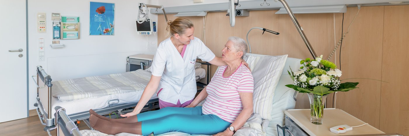 Eine Krankenpflegerin hilft einer älteren Dame beim Aufstehen aus dem Krankenhausbett