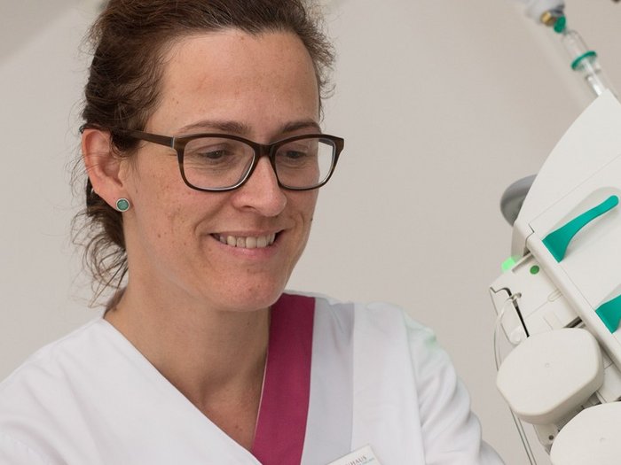 Eine Ärztin mit Brille schaut auf einen Behandlungsplan, sie lächelt, im Hintergrund Büroordner