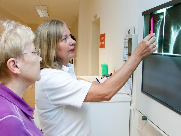 Eine Ärztin erkärt einer älteren Patientin Röntgenbilder an einer Tafel.