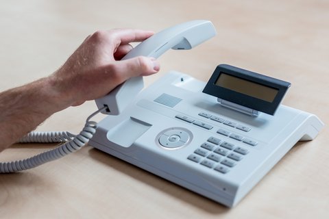 Eine Hand legt einen Hörer auf ein Telefon